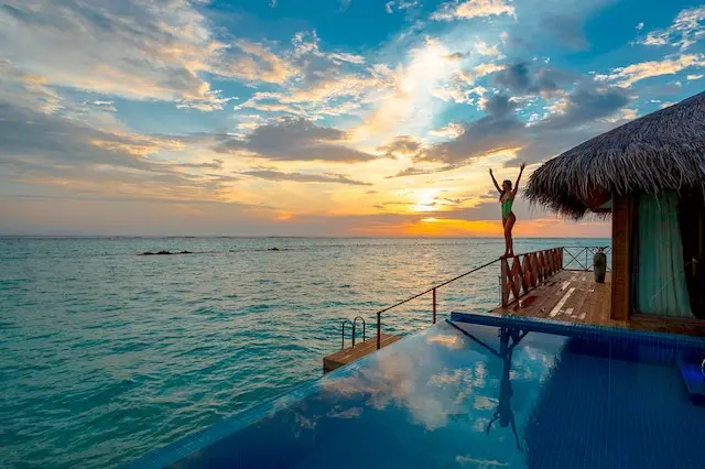 Opção de hospedagem para as férias na praia. Para evitar gastos com hotéis, a multipropriedade é uma alternativa. Imagens de mulher na varanda de um hotel tropical na praia, pô do sol ao fundo. Foto de Asad Photo Maldives.