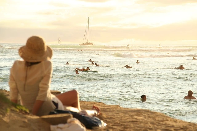 Lugares com praia são os destinos preferidos para quem quer descansar nas férias de verão. Imagem de mulher descansando na areia da praia, enquanto observa o mar e o pôr do sol. Foto DPUNG por Pixabay.