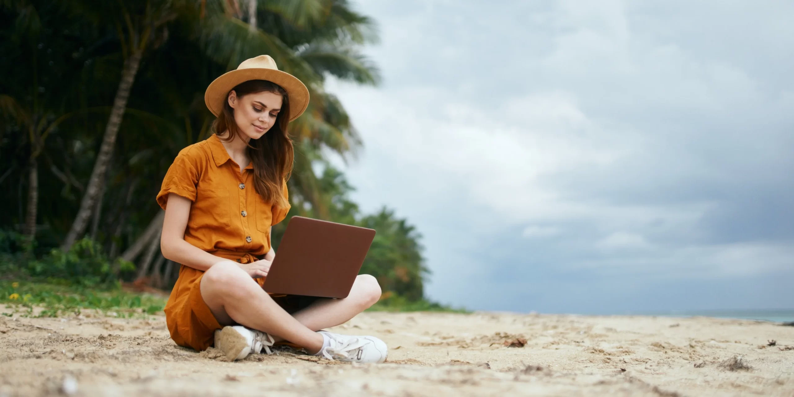 Tendência de nomadismo digital. Na imagem, mulher realiza trabalho remoto, com notebook, na Praia. Praia de Pipa é um dos destinos que está na rota dos Nômades Digitais